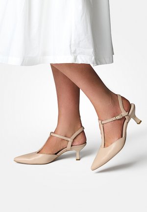 Escarpins beige à bout pointu et brides arrière avec un design en T, petits talons carrés et finition en cuir lisse. Accentué par des sangles de cheville réglables.