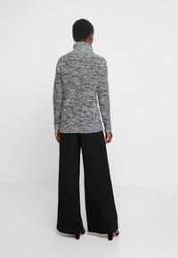 Grauer und weißer melierter Strickrollkragenpullover, lange Ärmel, gerippte Bündchen, kombiniert mit schwarzen weit geschnittenen Hosen und schlichten schwarzen High Heels.