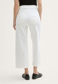 Pantaloni bianchi a gamba larga con vita alta, due tasche posteriori e taglio dritto. Il tessuto sembra leggero e con una texture. Scarpe nere completano il look.