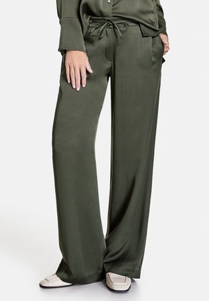 Mujer vistiendo pantalones anchos de color verde oliva con cintura ajustable con cordón y mocasines beige claro, manos descansando cerca de los bolsillos.