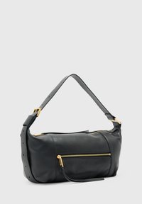 Sac à épaule en cuir noir avec bandoulière réglable, fermeture éclair dorée sur la poche avant et le compartiment principal, présenté sur un fond clair uni.