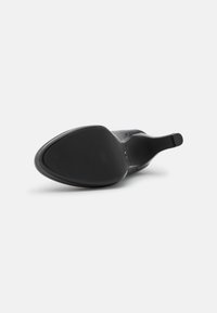 Botte noire à talon haut et bout pointu, couchée sur le côté, montrant la semelle et le talon fin sur fond blanc.