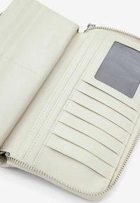 Šviesiai kreminės odos piniginės vidus su keliais kortelių lizdais ir aiškiu ID langeliu. Yra užtrauktukas ir subtilūs siuvinėjimo detalės.