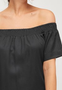 Top nero fuori spalle con scollatura arricciata, maniche corte e una superficie di tessuto liscia, caratterizzato da una vestibilità rilassata e un design minimalista.
