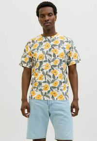 Tricou cu mânecă scurtă, de culoare albă, cu un model floral ce include trandafiri galbeni și frunze verzi. Asortat cu pantaloni scurți din denim albastru deschis.