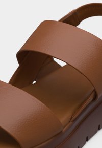 Καφέ δερμάτινο σανδάλι με δύο φαρδιές λουριά και χοντρή, υφασμένη σόλα.