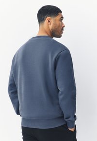 Texturált anyagból készült tengerészkék pulóver, kerek nyakkal és bordázott mandzsettákkal. A hátoldalon egyszerű, letisztult mintázat található.