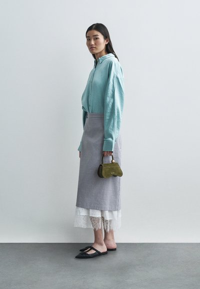 Γαλάζιο πουκάμισο με κουμπιά, γκρι φούστα με δαντελένια τελειώματα, μαύρες επίπεδες παπούτσια και μικρή πράσινη τσάντα χεριού. Απλός σχεδιασμός, μαλακά υλικά και επιμερισμένα υφάσματα.