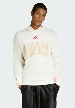 White hoodie featuring large beige "ADIDAS" text, red logo above. Soft fabric with a relaxed fit, paired with black shorts.