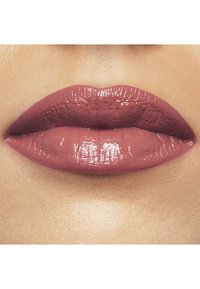 Rosa Lippenstift mit glänzendem Finish, auf vollen Lippen aufgetragen. Glatte Textur mit sichtbaren feinen Linien, vor einem neutralen Hautton-Hintergrund.