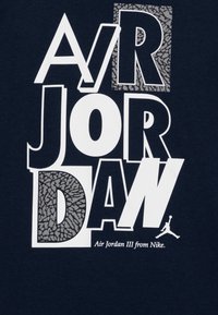 Námořnické bavlněné tričko s výrazným bílým a šedým textem "AIR JORDAN", s texturovaným vzorem v písmenu "D" a malou ikonou loga.