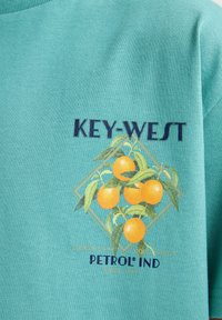 Tyrkysové bavlněné tričko s grafickým designem pomerančů a zelených listů, spolu s textem "KEY-WEST" a "PETROL IND".