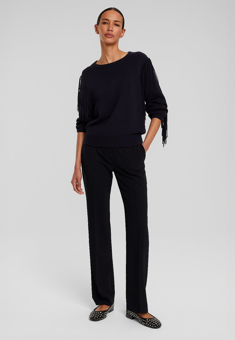 Maglione blu navy con dettagli in frange sulle maniche, abbinato a pantaloni neri e ballerine nere con borchie argentate. Tessuto dalla superficie liscia.