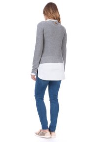 Maglione grigio lavorato a maglia con maniche lunghe, con un colletto bianco sotto, indossato sopra jeans blu. La vista posteriore mostra un design con fessura laterale.