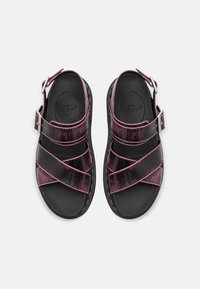 Black and pink strappy sandals with a matte finish, featuring a buckle closure, padded footbed, and signature yellow stitching along the sole.
