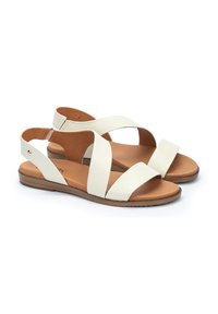 Sandalias de cuero blanco con tiras entrelazadas, espalda abierta y suela marrón. Textura suave y diseño plano, adecuadas para un uso casual.