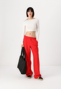 Crop top blanc à manches longues, pantalon rouge à larges jambes, sac fourre-tout noir et baskets noires avec une semelle claire. Tissu lisse, coupe décontractée.