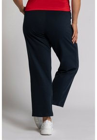 Mörkblå elastiska midjebyxor med en lös passform, slät textur och vida ben. Matchas med vita sportskor för en avslappnad look.