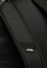 Czarny pasek na ramię do plecaka, wykonany z teksturowanej tkaniny z wzmocnioną krawędzią; posiada małą białą metkę z logo z napisem "SUPERORY".