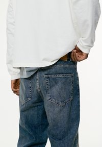 Dunkelblaue Jeans aus Denim mit lockerer Passform, leicht ausgebleicht, ausgestattet mit zwei Gesäßtaschen und einem braunen Lederlabel an der Taille.