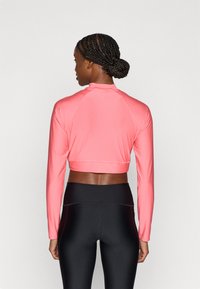 Ροζ cropped μπλούζα με μακριά μανίκια, με λαιμόκοψη ψηλή, υφασμάτινη υφή και λεπτομέρειες με ραφές. Συνδυασμένη με μαύρο κολάν με ψηλή μέση.