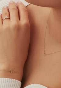 De gouden juwelenset bevat een ring met een heldere steen, een hartvormige armband en een hart hanger aan een delicate keten, allemaal met een gepolijste afwerking.