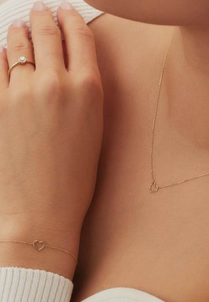 Das Goldschmuckset umfasst einen Ring mit einem klaren Stein, ein herzförmiges Armband und einen Herzanhänger an einer zarten Kette, die alle mit einer polierten Oberfläche versehen sind.