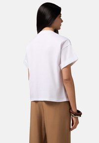 Witte T-shirt met korte mouwen, relaxed fit, ronde hals en opgerolde mouwen, gecombineerd met lichtbruine geweven wijde broek.