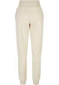 Beige Jogginghose mit geripptem Taillenbund und Knöchelbündchen. Glatte Textur, schmal zulaufendes Bein Design, mit Taschen an den Seiten.