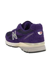 Zapatilla deportiva morada con parte superior de ante texturizado, paneles de malla y logo blanco. Presenta una suela ligera con un sutil detalle de amortiguación.
