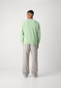 Green sweatshirt with a crew neck and ribbed cuffs, paired with light gray, loose-fitting pants and neutral-colored shoes.
