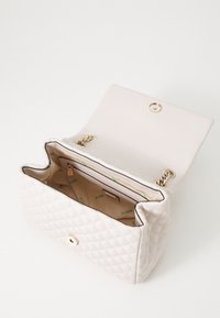 Bolso blanco acolchado con herrajes dorados, cierre a presión y un bolsillo interior con cremallera. El interior forrado presenta un sutil estampado de logo.