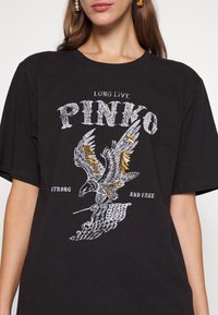 Černé bavlněné tričko s výraznou grafikou orla s kovovými akcenty a textem "DLOUHO ŽIJ PINKO" a "SILNÝ A SVOBODNÝ" v opotřebované bílé.