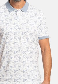 Polo de manga corta en azul claro y blanco, con un patrón detallado de árboles y animales. Tejido suave con cuello tipo polo y mangas con puños.
