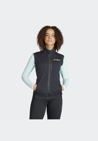Black sleeveless vest with zippered front, light blue long sleeves featuring text print, breathable material, and side pockets.