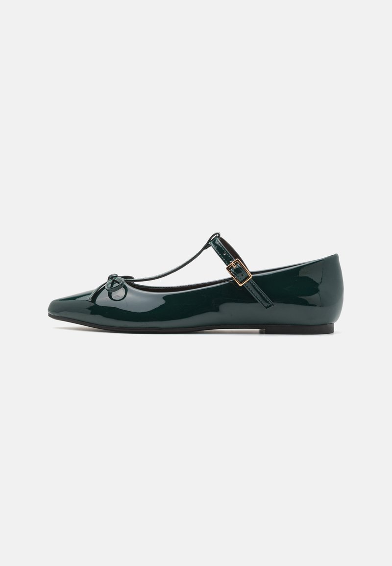 Green patent leather flat shoe with a pointed toe, T-strap, and decorative bow detail. Features a small buckle and low profile heel.