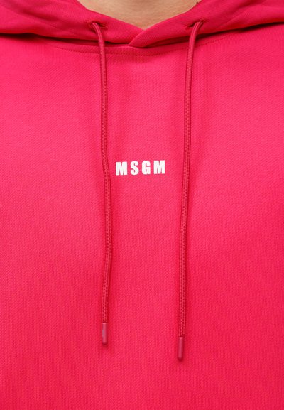 Φωτεινή ροζ μπλούζα με κουκούλα με το λευκό λογότυπο MSGM στο κέντρο κάτω από τον λαιμό και ροζ κορδόνια που κρέμονται.