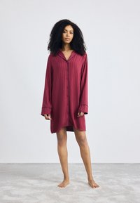 Vestito da pigiama bordeaux con colletto, maniche lunghe e chiusura con bottoni; presenta righe verticali e polsini a contrasto.