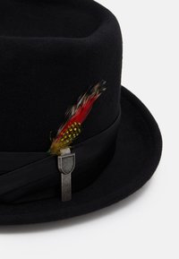 Chapeau en feutre noir à large bord, avec un ruban noir et un accent de plume colorée maintenu par un clip en argent.