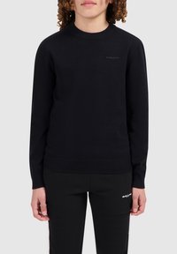 Zwart gebreid sweater met een ronde hals en geribde manchetten, voorzien van een subtiele logo op de borst. Draagt bij zwarte broek.