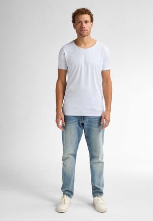 Witte T-shirt met korte mouwen en ronde hals, gedragen met lichtblauwe spijkerbroek en witte sneakers. Glad materiaal en casual pasvorm.