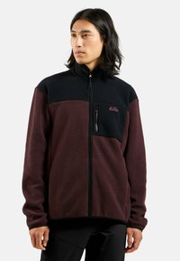 Fleece jacket in dark maroon with black paneling. Features zippered chest pocket and high collar. Textured fabric and relaxed fit.