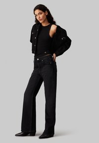 Black denim jacket with silver buttons, black tank top, and wide-leg black jeans. Black pointed ankle boots. Clean, minimalist design.