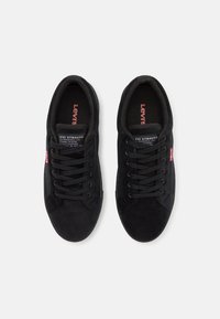 Black suede sneakers with round toe, textured laces, and a logo on the tongue. Side features a small red label. Flat rubber sole.