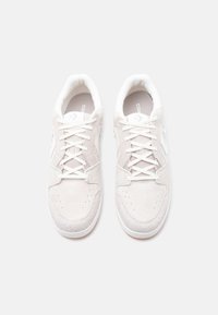 Ζευγάρι μπεζ σουέτ αθλητικά παπούτσια με λευκά κορδόνια και ελαστικές σόλες, φωτογραφημένα από πάνω σε λευκό φόντο.