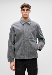 Grau melierte Wollmischjacke mit einem Kragen, einer einzelnen Brusttasche und weiten Ärmeln. Strukturiertem Stoff mit weicher Oberfläche.