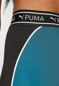 La fascia elastica PUMA in nero presenta un logo. I leggings in teal e nero mostrano texture contrastanti e un dettaglio in piping bianco.
