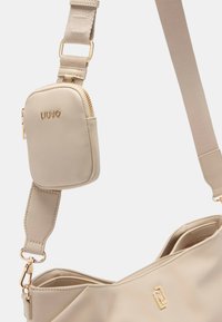Borsa beige con una texture liscia, dotata di una piccola pochette rimovibile. Accenti in metallo dorato e una larga tracolla regolabile.