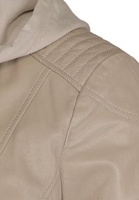 Beige läderjacka med kviltad axeldesign och kontrasterande beige tyghuva. Har synlig sömnad och en slät textur.