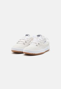 Adidași din suede alb, cu o talpă din cauciuc, având șireturi albe, detalii perforate și un logo negru pe limbă.